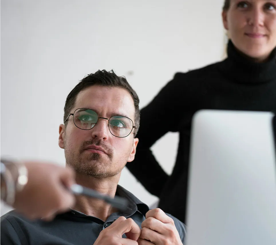 man looking away from computer to a person speaking to them